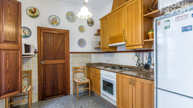 Rustikale Küche mit Holzschränken, Granit-Arbeitsfläche, Gasherd, Kühlschrank und dekorativen Keramiktellern an der Wand.
