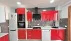 Cocina empotrada moderna con frentes rojos de alto brillo, lavavajillas y combi frigorífico-congelador en apartamento renovado
