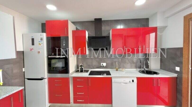 Cocina empotrada moderna con frentes rojos de alto brillo, lavavajillas y combi frigorífico-congelador en apartamento renovado