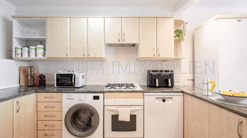 Cocina luminosa con frentes de madera, estufa de gas, lavadora, lavavajillas y microondas en apartamento en primera línea de mar Port Adriano.