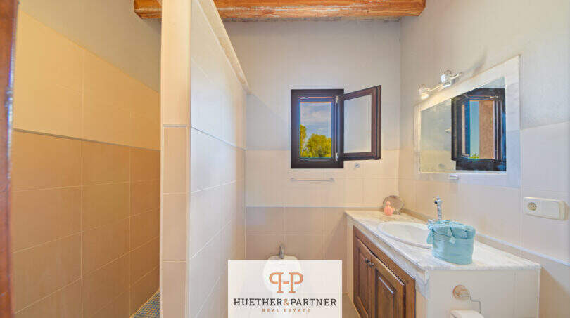 Badezimmer der Finca Felanitx mit Waschbecken, Bidet, Holzbalkendecke und kleinem Fenster mit Naturblick