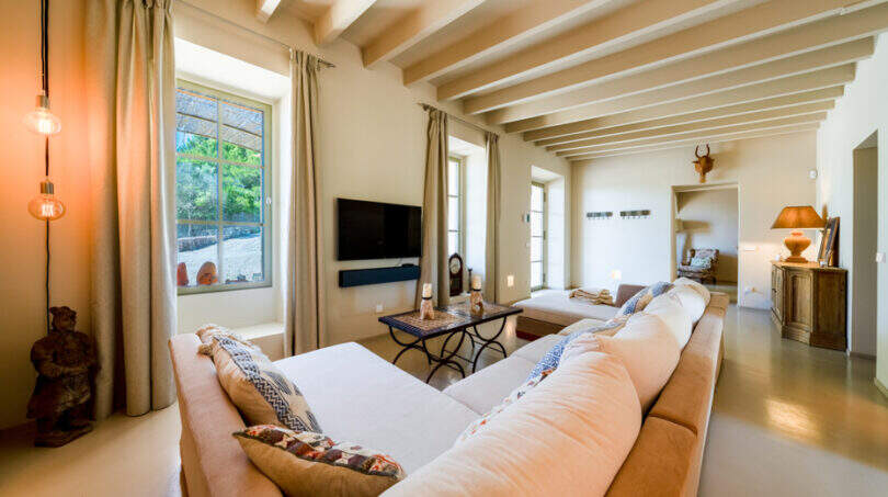 Helles Wohnzimmer der Finca in Esporles mit Holzbalkendecke, großem Ecksofa und mediterranem Ambiente.