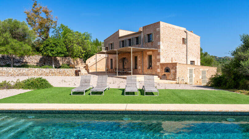 Rustikale Naturstein-Finca in Cales de Mallorca mit türkisem Pool, Liegestühlen und gepflegtem Gartenbereich.