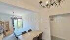 Luminosa zona de estar-comedor con mesa de madera, sillas marrones y lámpara de araña en apartamento renovado en Palma
