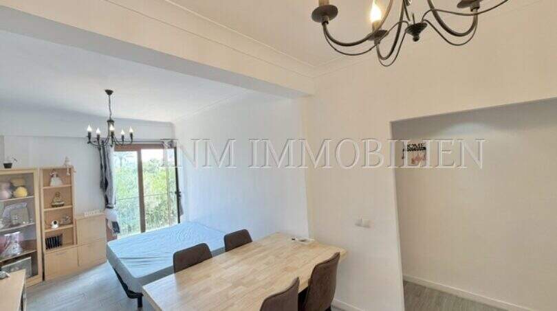 Luminosa zona de estar-comedor con mesa de madera, sillas marrones y lámpara de araña en apartamento renovado en Palma