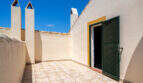 Sonnige Dachterrasse mit Fliesenbelag, weißen Schornsteinen und grüner Holztür in Cala Murada
