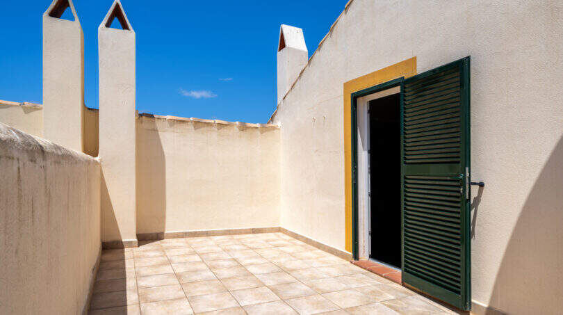 Sonnige Dachterrasse mit Fliesenbelag, weißen Schornsteinen und grüner Holztür in Cala Murada