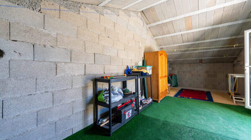 Garage mit Betonwänden, Holzschrank, Regalen und grünem Kunstrasenboden in Doppelhaus Cala Murada