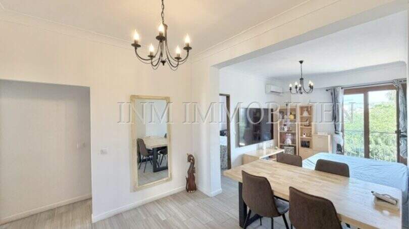 Luminosa zona de comedor y sala de estar del apartamento renovado en Palma con mesa de madera, lámpara de araña y ventana con vista al mar