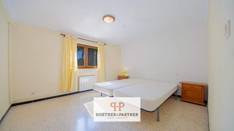 Helles Schlafzimmer der Finca Son Macià mit zwei Einzelbetten, Holzmöbeln und gelbem Vorhang