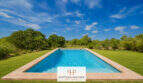 Rechteckiger Pool mit Natursteinrand, umgeben von grüner Wiese und mediterranem Grün der Finca bei Felanitx