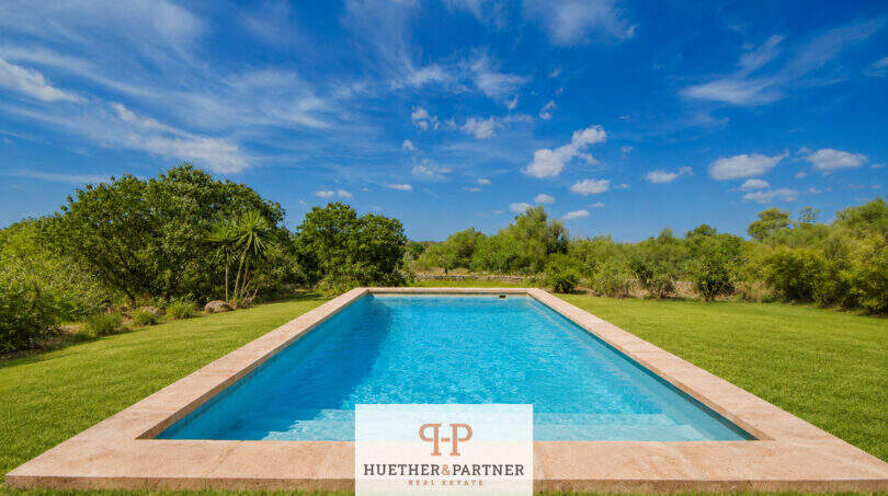 Rechteckiger Pool mit Natursteinrand, umgeben von grüner Wiese und mediterranem Grün der Finca bei Felanitx