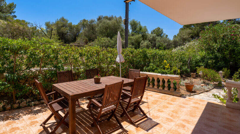 Sonnige Terrasse mit Holzmöbeln und üppigem Grün in Cala Murada