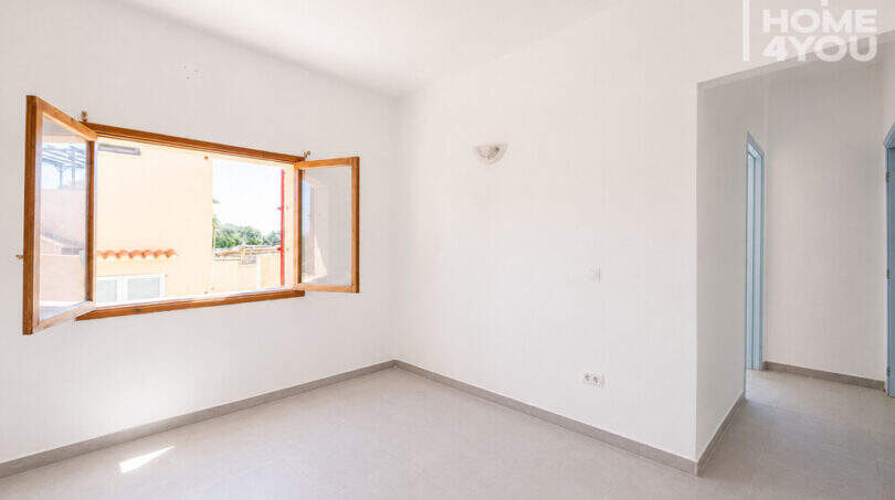 Helles leeres Schlafzimmer mit Holzfenster, weißen Wänden und Fliesenboden in Erdgeschosswohnung Cala Llombards