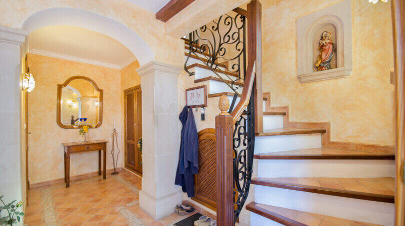 Eleganter Eingangsbereich der Finca Son Macià mit geschwungener Holztreppe, Schmiedeeisen-Geländer und mediterranem Flair.