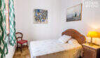 Schlafzimmer mit Holzbett, Nachttisch, Lampe, Wandgemälden und grünen Ikat-Vorhängen im historischen Herrenhaus Porreres