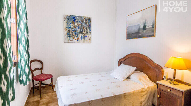 Schlafzimmer mit Holzbett, Nachttisch, Lampe, Wandgemälden und grünen Ikat-Vorhängen im historischen Herrenhaus Porreres