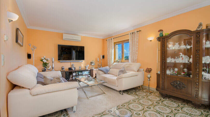 Helles Wohnzimmer der Finca in Son Macià mit cremefarbenen Sofas, Vitrine und gemustertem Fliesenboden.