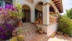 Entrada a la villa de Cala Murada con arcadas, escalones de terracota, buganvillas y plantas mediterráneas en macetas.