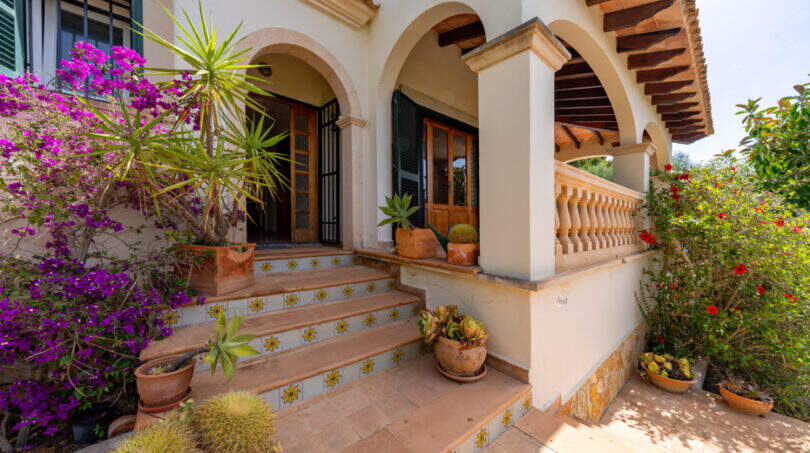 Entrada a la villa de Cala Murada con arcadas, escalones de terracota, buganvillas y plantas mediterráneas en macetas.