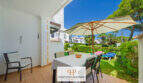 Überdachte Terrasse mit Esstisch und Sonnenschirm, Blick auf gepflegten Gartenbereich der Anlage in Cala d'Or.