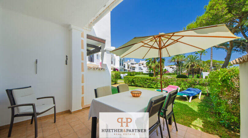 Überdachte Terrasse mit Esstisch und Sonnenschirm, Blick auf gepflegten Gartenbereich der Anlage in Cala d'Or.