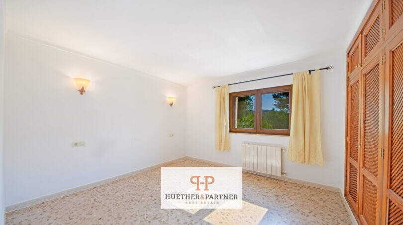Helles Schlafzimmer der Finca Son Macià mit Holzeinbauschrank, gelbem Vorhang und Blick ins Grüne.