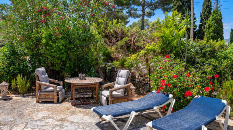 Sonnenterrasse mit Liegestühlen, Holzmöbeln und üppigem Blumengarten des Erdgeschossapartments in Cala Murada.