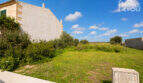 Urbanes Baugrundstück 391 m² in Ses Salines mit Grünfläche, Olivenbäumen und angrenzendem Steinhaus unter blauem Himmel.