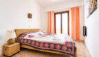 Helles Schlafzimmer mit Doppelbett, Rattan-Möbeln, orangefarbenen Vorhängen und Balkontür, Ferienwohnung Ses Salines