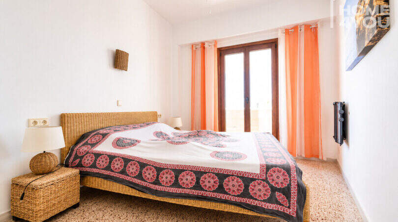 Helles Schlafzimmer mit Doppelbett, Rattan-Möbeln, orangefarbenen Vorhängen und Balkontür, Ferienwohnung Ses Salines