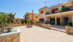 Gepflasterte Terrasse mit Steinbalustrade vor mediterranem Wohnkomplex mit roten Fensterläden in Cala Llombards