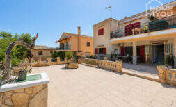 Gepflasterte Terrasse mit Steinbalustrade vor mediterranem Wohnkomplex mit roten Fensterläden in Cala Llombards