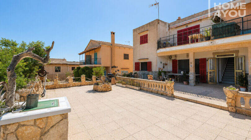 Gepflasterte Terrasse mit Steinbalustrade vor mediterranem Wohnkomplex mit roten Fensterläden in Cala Llombards