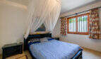 Dormitorio de la villa de Cala Murada con cama con dosel, ropa de cama azul y blanca y una mosquitera decorativa.
