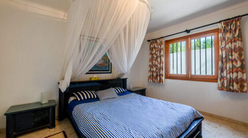 Dormitorio de la villa de Cala Murada con cama con dosel, ropa de cama azul y blanca y una mosquitera decorativa.