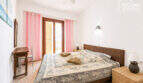 Helles Schlafzimmer mit Doppelbett, Rattan-Möbeln, Deckenventilator und Balkontür mit rosa Vorhängen.