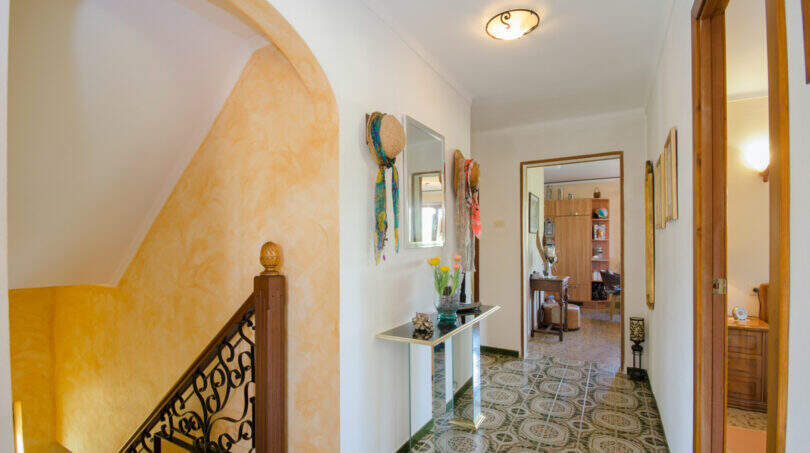 Heller Flur der Finca in Son Macià mit Mosaikboden, Bogennische, Holztreppe und dekorativem Wandspiegel