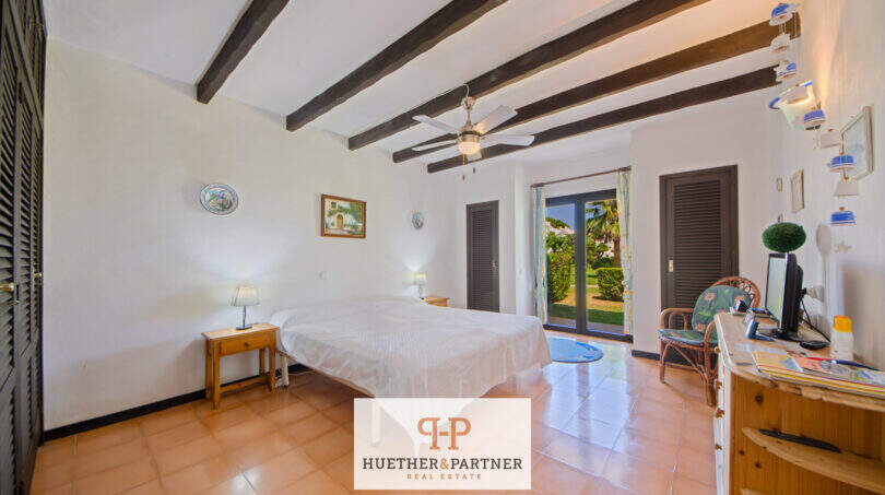 Helles Schlafzimmer mit Terrakottaboden, Holzbalken, Deckenventilator und Terrassentür zum Garten.