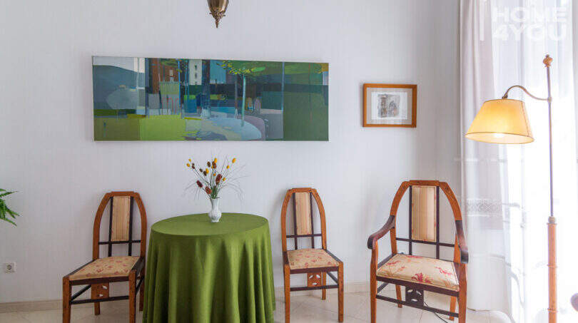 Elegantes Wohnzimmer im Herrenhaus Porreres mit antiken Holzstühlen, grünem Rundtisch und Gemälde an weißer Wand