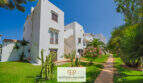 Außenansicht der weißen Apartmentanlage in Cala d'Or mit gepflegtem Garten, Palmen und Kakteen.