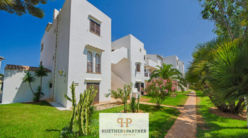 Außenansicht der weißen Apartmentanlage in Cala d'Or mit gepflegtem Garten, Palmen und Kakteen.