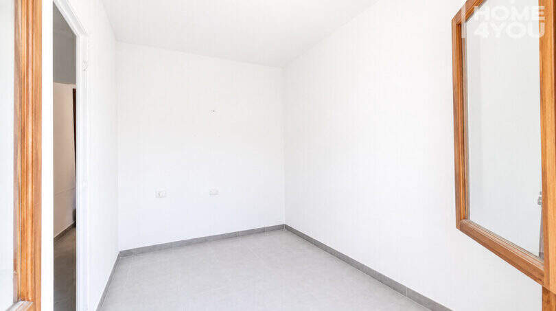 Leeres Schlafzimmer mit Fliesenboden, weißen Wänden und Holzrahmen-Fenster in Erdgeschosswohnung Cala Llombards