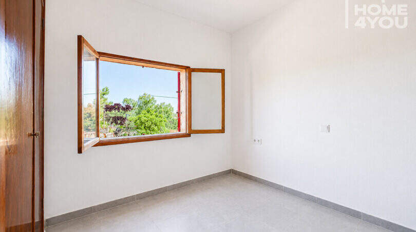 Helles leeres Zimmer mit Holzfenster und Gartenblick in Erdgeschosswohnung Cala Llombards, Fliesenboden