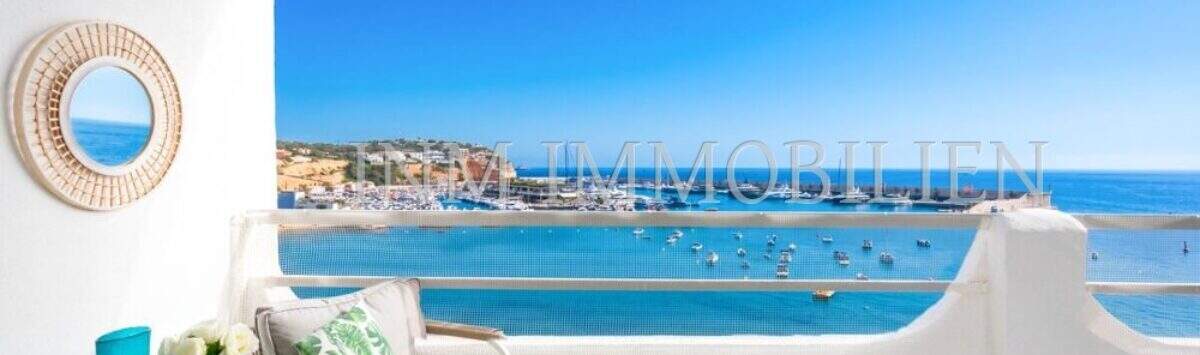 Terraza soleada del apartamento frente al mar en Port Adriano con vistas al mar, puerto y muebles de estar elegantes.