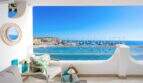 Terraza soleada del apartamento frente al mar en Port Adriano con vistas al mar, puerto y muebles de estar elegantes.