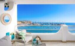 Terraza soleada del apartamento frente al mar en Port Adriano con vistas al mar, puerto y muebles de estar elegantes.