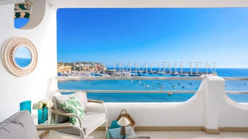 Terraza soleada del apartamento frente al mar en Port Adriano con vistas al mar, puerto y muebles de estar elegantes.