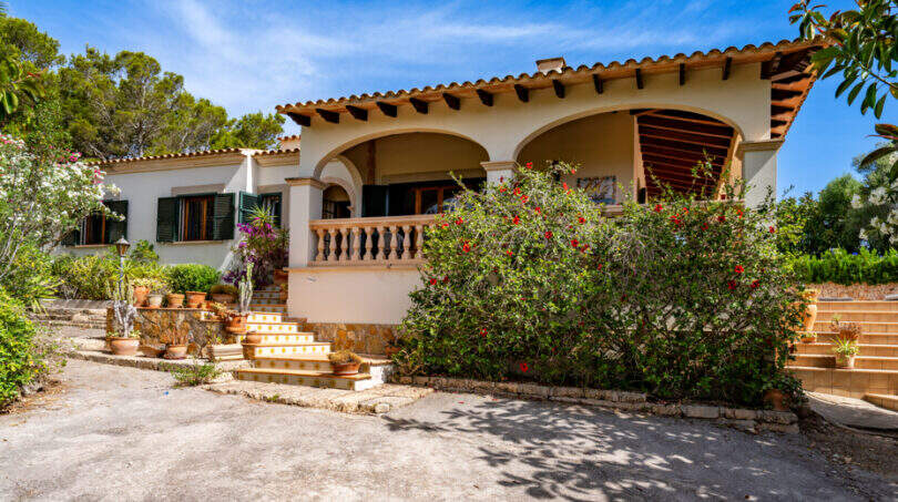 Vista exterior de una villa mediterránea en Cala Murada con terraza abovedada, escalera y exuberante vegetación en flor
