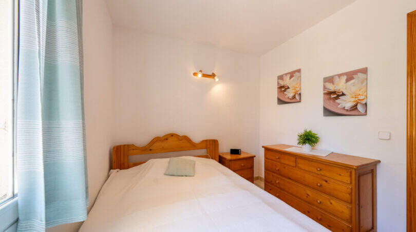 Helles Schlafzimmer mit Doppelbett, Holzmöbeln und mintgrünen Vorhängen im Doppelhaus Cala Murada